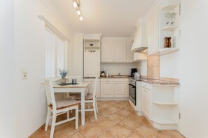 A compact kitchen with white cabinetry, a dining table with chairs, and a tiled floor.