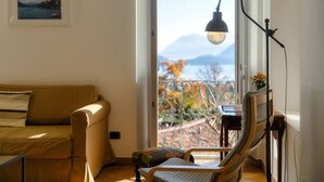 Una sala de estar con un sofá, una silla, una mesa, una lámpara y vistas a un balcón con barandilla.