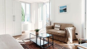 Un salón luminoso con una mesa de centro de vidrio, un sofá beige y vistas a la vegetación a través de la ventana.