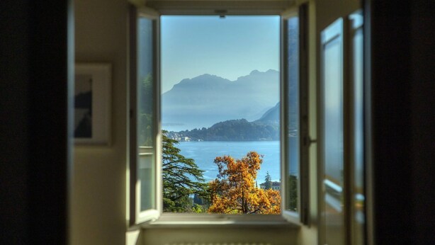 Una ventana con vista a un lago, montañas y follaje otoñal.
