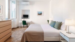 Een hotelkamer met een bed, een bureau met een computer, een stoel, een dressoir, een raam en een schilderij aan de muur.