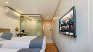 Ein Hotelzimmer mit zwei Betten, einem Couchtisch, einem an der Wand befestigten Fernseher und einer Klimaanlage.