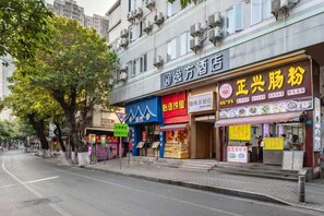 Straßenansicht mit einem Hotel und verschiedenen Geschäften, darunter ein Restaurant mit einer auffälligen, gelben Beschilderung.