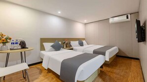 Ein Hotelzimmer mit zwei Betten, einem kleinen Tisch mit einer Blumenvase und einer Klimaanlage an der Wand.