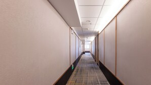 Ein langer, schmaler Korridor mit einem gemusterten Teppich, Holzvertäfelung an den Wänden und einer Decke mit eingelassenen Leuchten.
