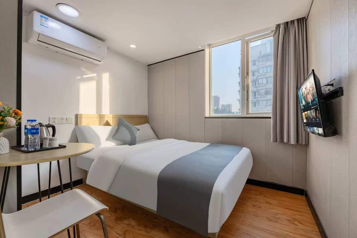 A hotel room with a bed, a desk, a chair, a TV, and a window with curtains.