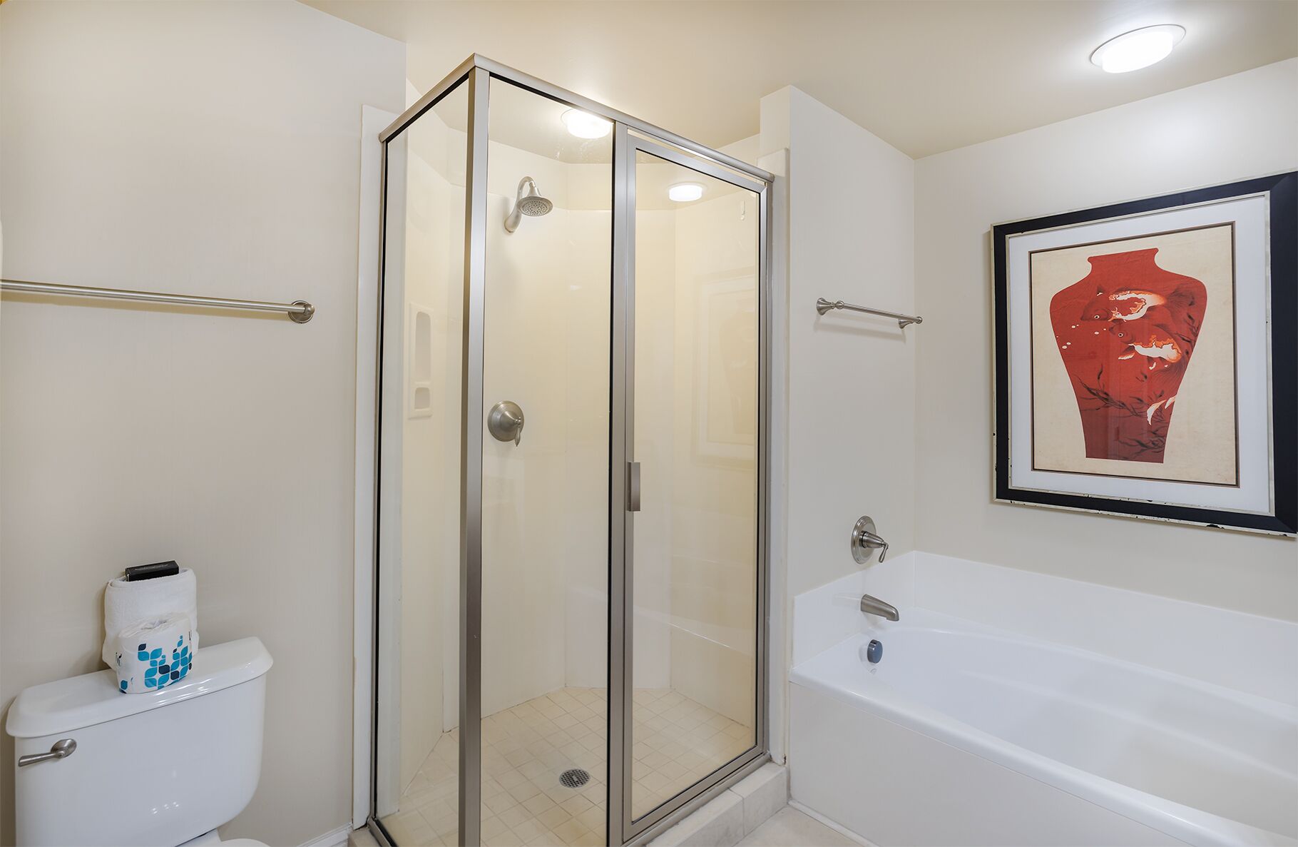 Une salle de bain avec une douche à parois de verre, des toilettes blanches ornées d’un motif bleu, une baignoire blanche et une œuvre d’art encadrée accrochée au mur.