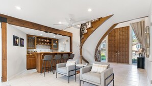 A modern kitchen with bar stools, a dining area with two sofas, and a staircase with a wooden finish. - Surreal Serenity Escape wIth Game Room, Pool & Spa (La Mesa)