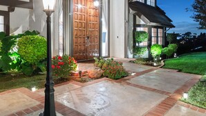 A two-story house with a prominent wooden front door, a well-lit front yard, and a clear night sky. - Surreal Serenity Escape wIth Game Room, Pool & Spa (La Mesa)
