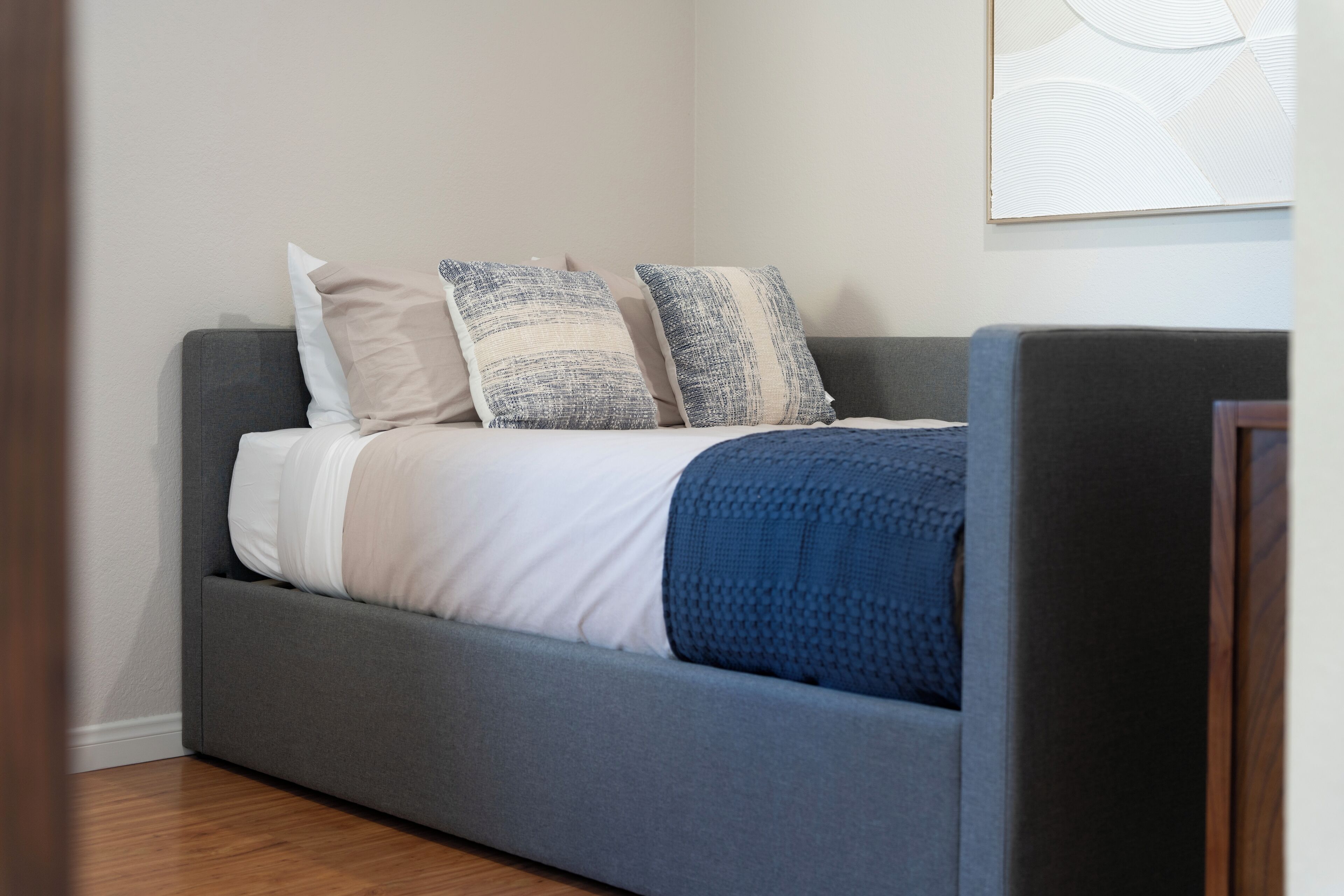 A modern bedroom with a grey sofa bed, white and blue pillows, and a blue blanket.