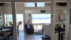 Un vaste espace de vie avec vue sur la plage, un coin repas avec une table et des chaises, et une cuisine équipée d’une cuisinière et d’un four.
