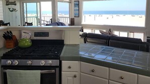 Une cuisine équipée d’une cuisinière, d’une bouilloire verte et offrant une vue sur la plage.