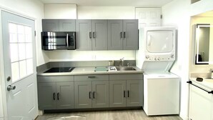 A modern kitchen with grey cabinets, a microwave, a sink, and a built-in washing machine.