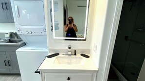 A modern bathroom with a white vanity, a large mirror, and a built-in washing machine.