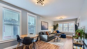 A modern living room with a wooden dining table, grey sofa, and a blue armchair.