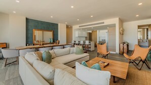 Ampla sala de estar com um sofá seccional grande, uma mesa de centro de madeira e uma área de jantar com cadeiras e mesa.