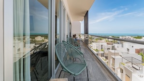 Uma varanda com duas cadeiras de vime, uma mesa e vista para o mar e edifícios.