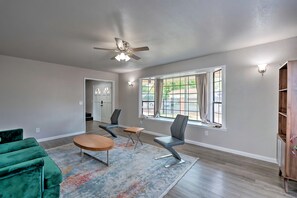 A spacious living room with a green sofa, a wooden coffee table, and a gray chair. There is a ceiling fan, a window with curtains, and a wooden cabinet. - Midcentury McMansion on 1 acre lot with Palm trees view (Sacramento)