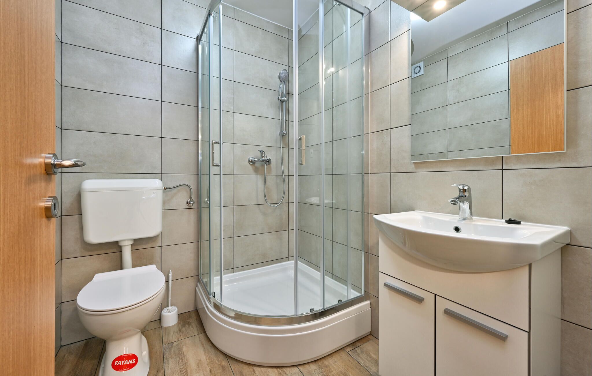 Un baño moderno con ducha envuelta en vidrio, inodoro blanco y lavamanos con espejo.