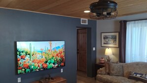 Uma sala de estar com uma televisão grande, móveis de madeira, um ventilador de teto e um quadro na parede.