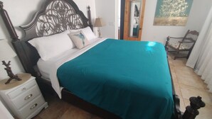 Cama bem arrumada com colcha verde-água, cabeceira de madeira e mesa de cabeceira com gavetas.