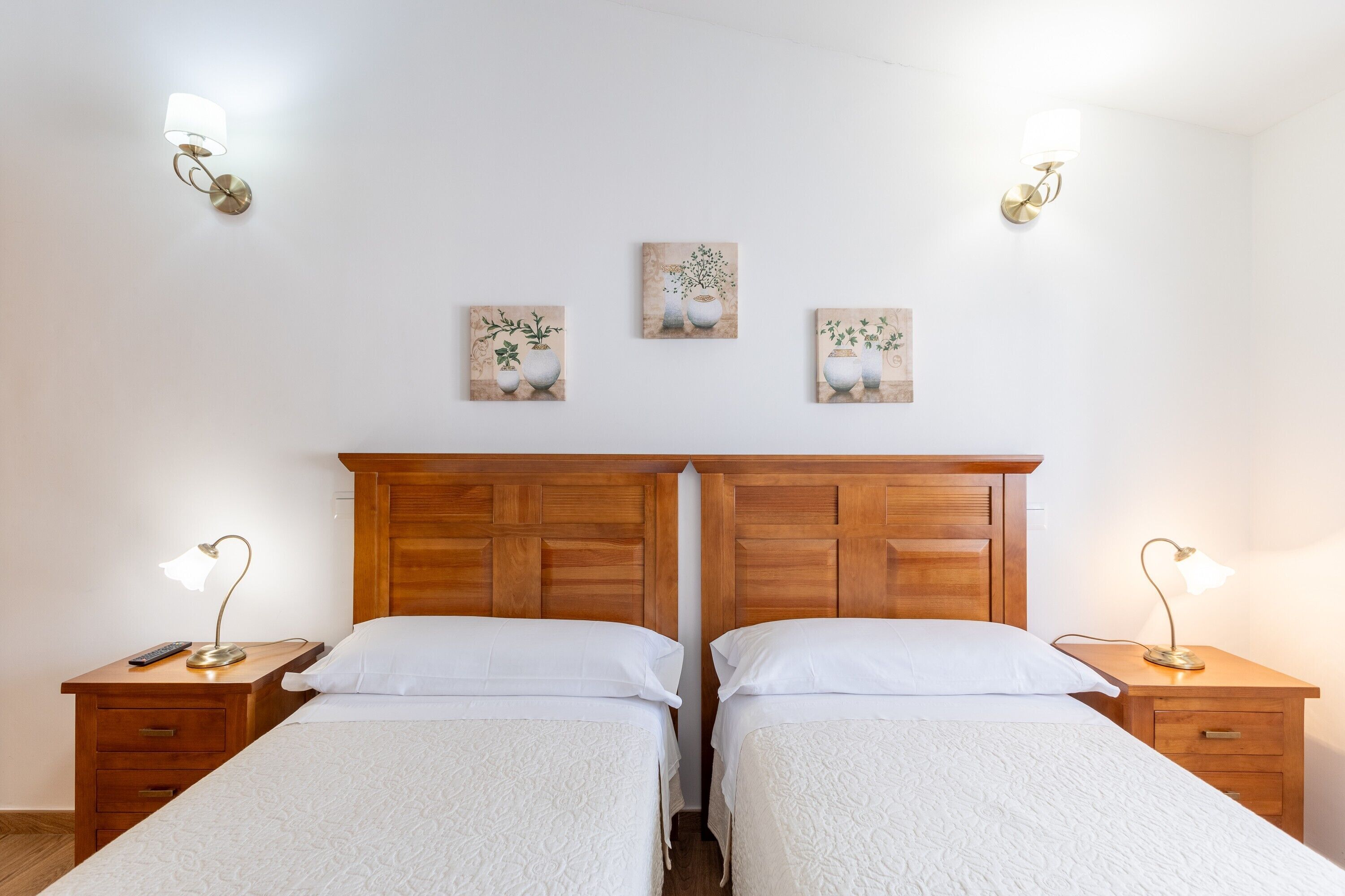 Una cama doble con cabecera de madera, dos mesitas de noche con lámparas y tres lámparas fijadas a la pared.
