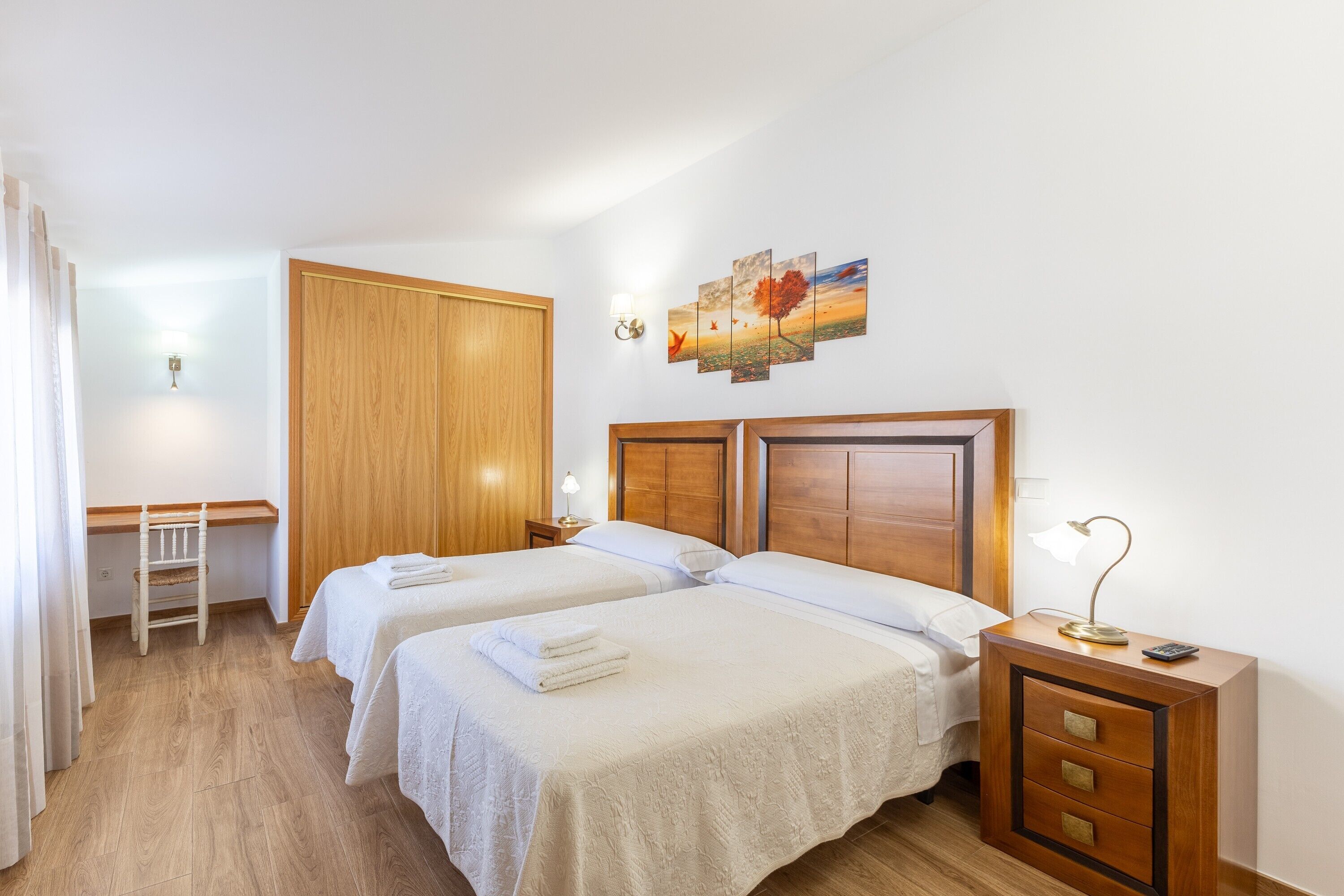 Habitación de hotel con dos camas, un escritorio, un armario y un cuadro en la pared.