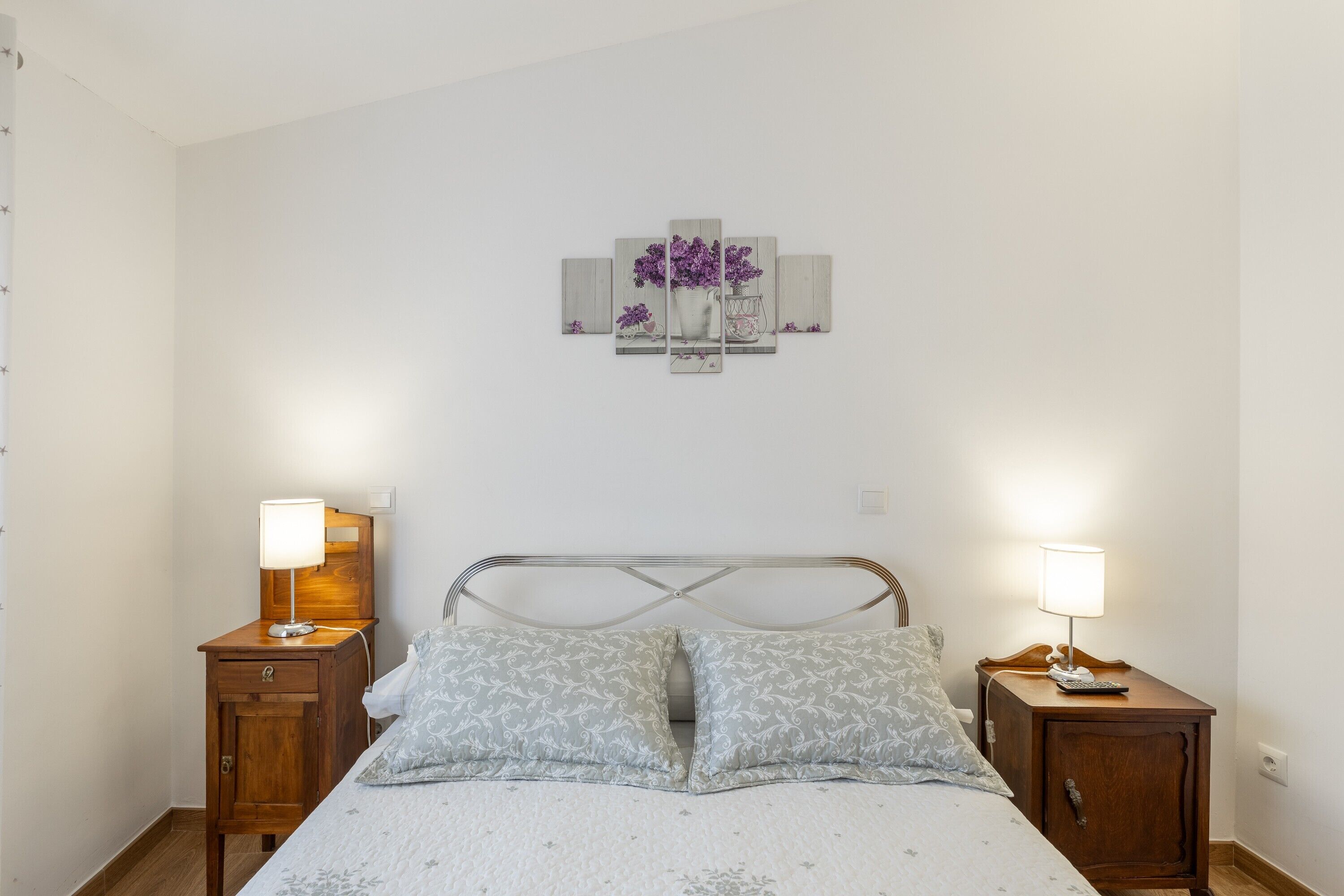 Una camera da letto con un letto, due comodini con lampade, un'opera d'arte appesa al muro e un tavolino da notte in legno.