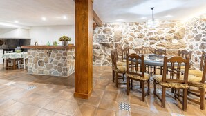 Un comedor con pared de piedra, sillas de madera, una mesa y una zona de bar con televisor.