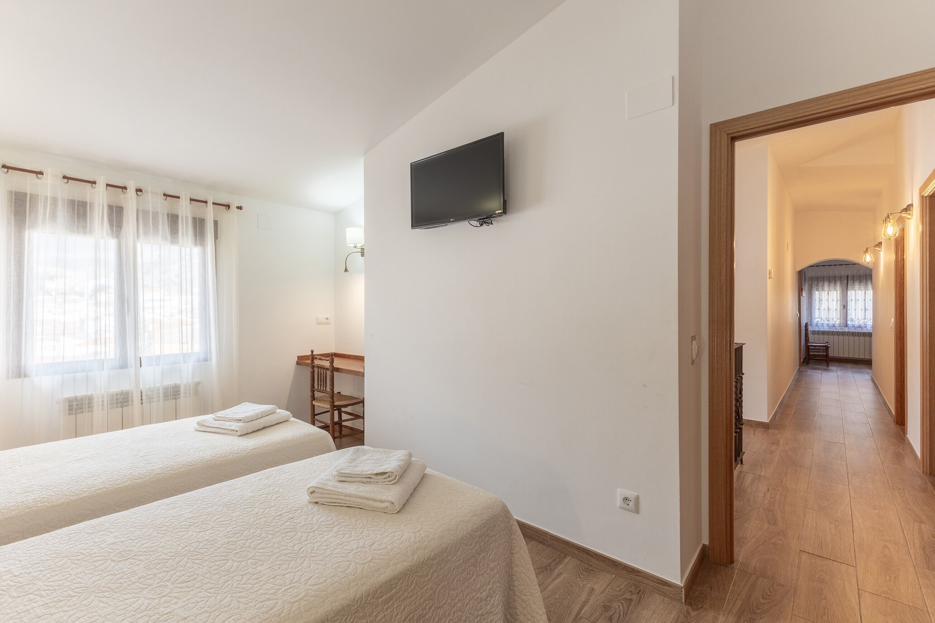 Habitació d'hotel amb dos llits, televisió, escriptori i vista a un passadís.