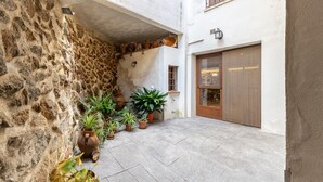 Un patio con paredes de piedra, plantas en macetas, suelo de baldosas y una puerta de madera.
