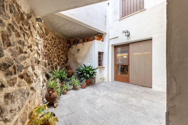 A courtyard with stone walls, potted plants, a tiled floor, and a wooden door.