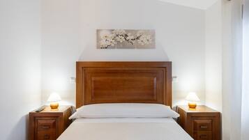Een netjes opgemaakt bed met een houten hoofdbord, twee nachtkastjes met lampen en een kunstwerk aan de muur erboven.