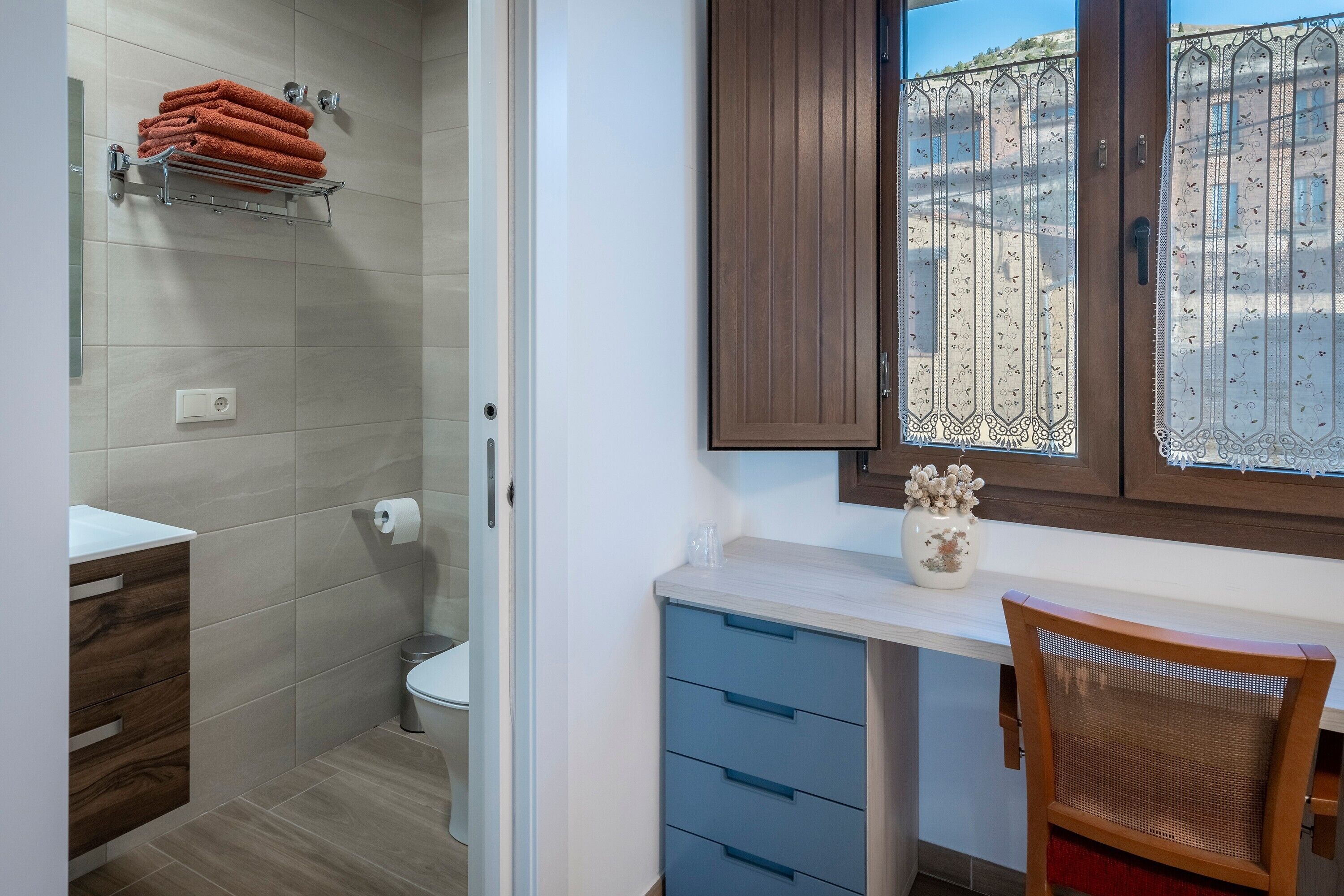 A bathroom with a toilet, a towel rack, a sink, and a window with a view of buildings.
