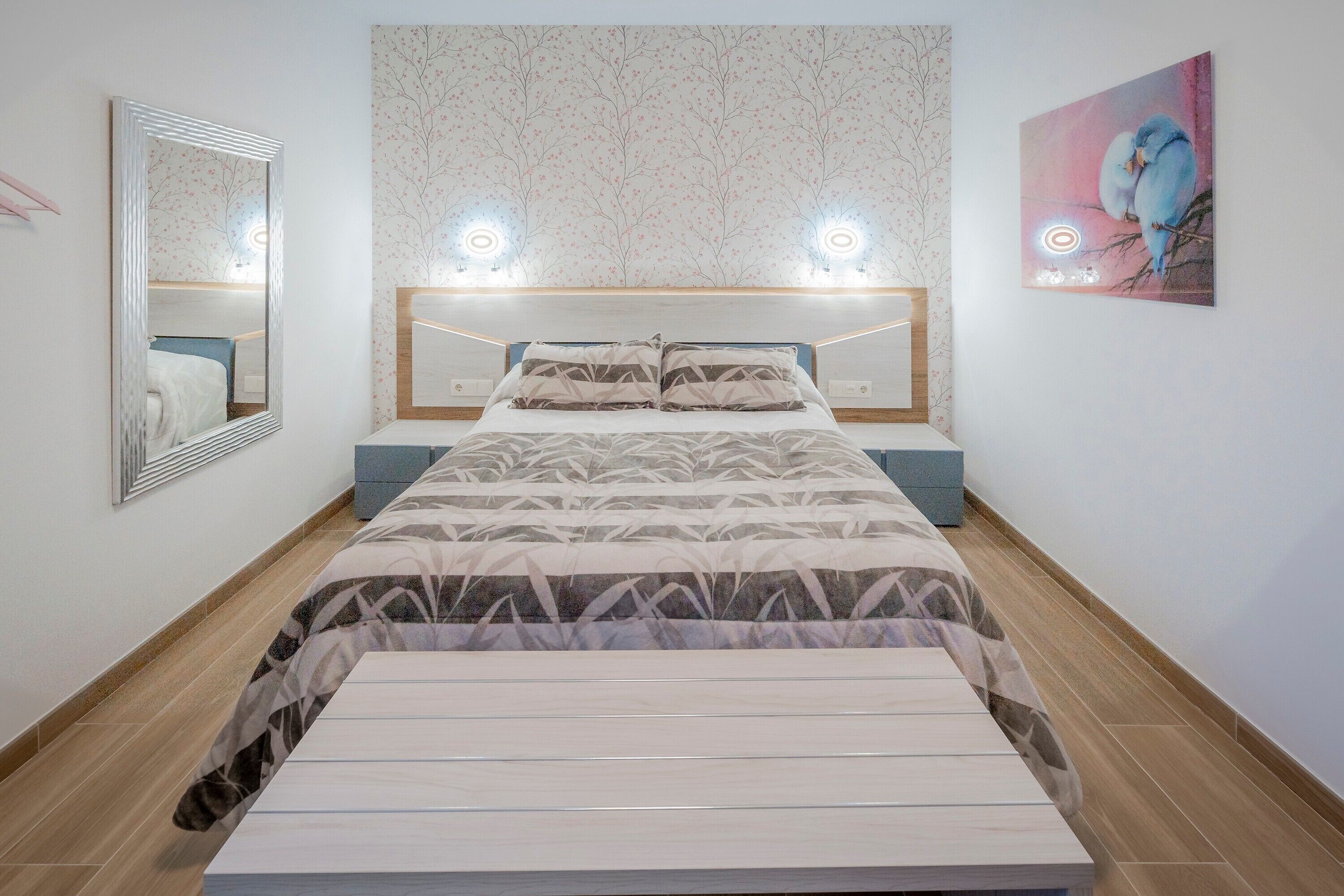 A bedroom with a bed, bedside tables, a mirror, and a wall-mounted artwork.
