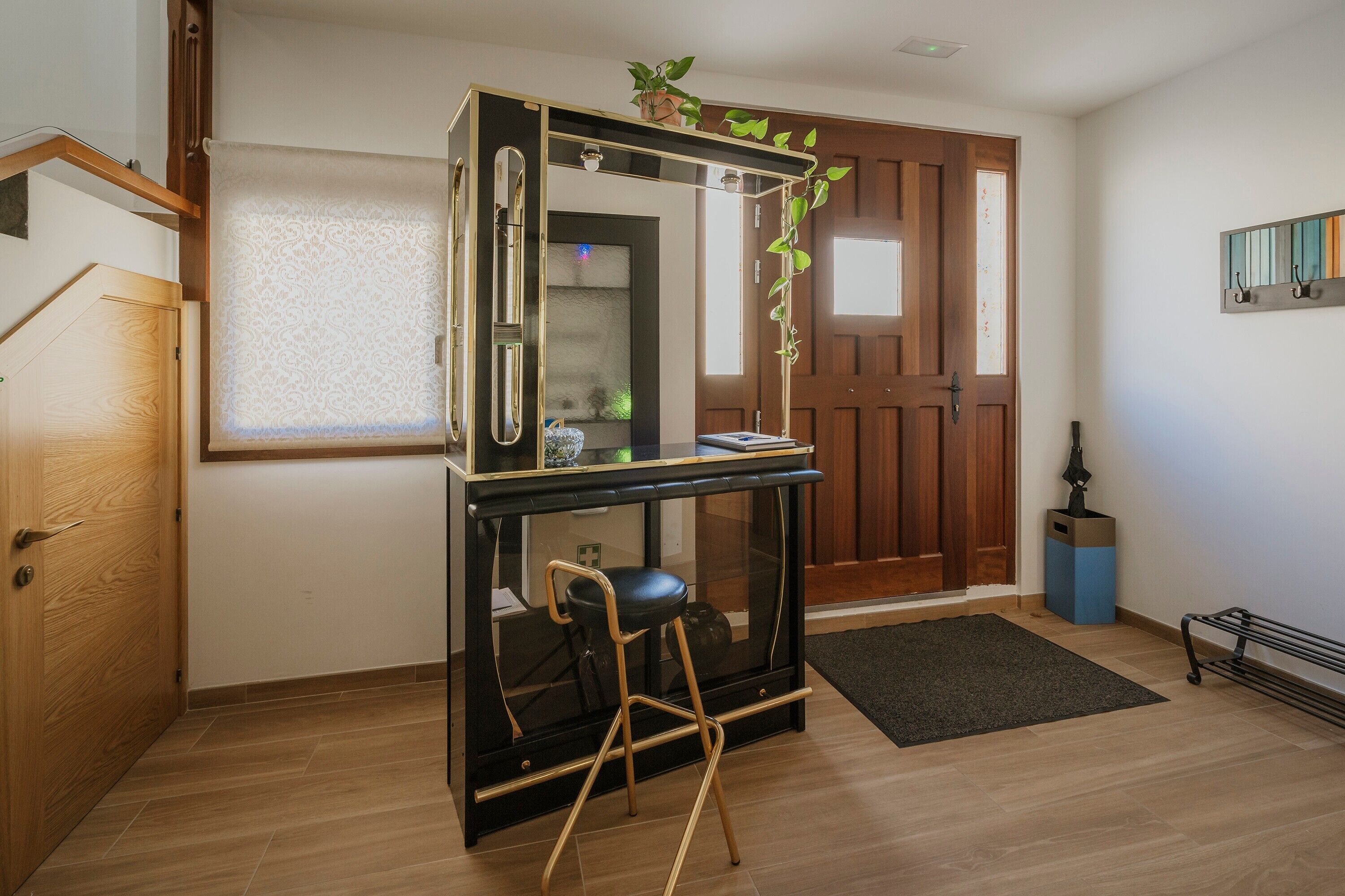Una habitación con puerta de madera, un escritorio negro con silla, una planta pequeña y un radiador.