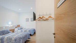 A hotel room with two beds, a TV, a coat rack, and a wooden door. - Country House 'Casa Rural El Rincon Del Chef' with Private Garden, Wi-Fi and Air Conditioning (Castrojeriz)
