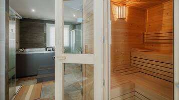 A modern bathroom with a glass shower enclosure, a wooden sauna, and a kitchen area visible through an open door.