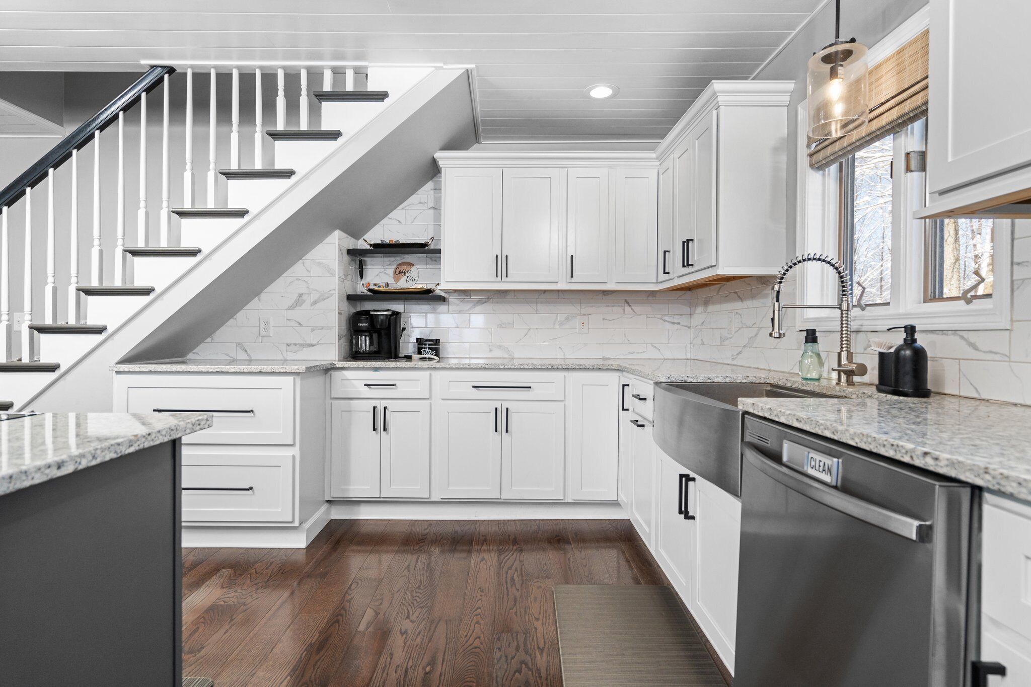 A modern kitchen with white cabinets, a stainless steel dishwasher, and a wooden staircase.