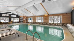 Ein Innenpool mit großen Glaswänden, Holzvertäfelung und Deckenventilator.