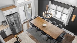 Eine moderne Küche mit einem Holzespeisetisch, schwarzen Stühlen, einem Edelstahlkühlschrank und einer Chandelüster.