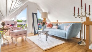 A spacious living room with a light blue sofa, a pink armchair, and a white table with a globe. A large mirror and a chandelier are also visible. - La petite maison bleue (Wandlitz OT Zerpenschleuse)