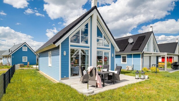 A blue house with a large glass window, a patio with outdoor furniture, and a neighboring red house. - La petite maison bleue (Wandlitz OT Zerpenschleuse)