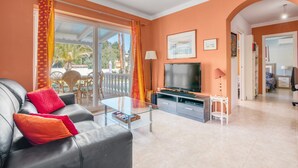 Ein Wohnzimmer mit einer Couch, einem Fernseher, einem Glastisch und einer Schiebetür zu einem Außenbereich.