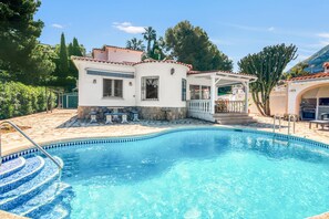 A swimming pool with a tiled edge, a white building with a balcony, and a patio area. - Villa 'Sophie' with Mountain View, Wi-Fi and Air Conditioning (Dénia)