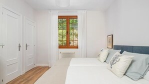 A bedroom with a bed, a window with curtains, a radiator, and white walls.