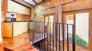 Una cocina con pared de piedra, un balcón con barandilla de metal y una ventana con cortinas.