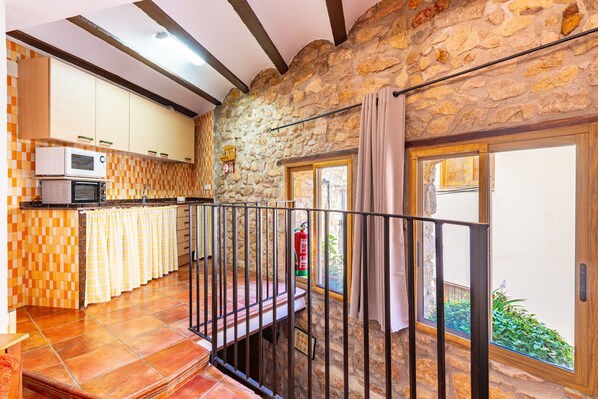 Une cuisine avec un mur en pierre, un balcon doté d’une rambarde en métal et une fenêtre avec des rideaux.