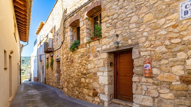 Una estrecha calle con edificios de piedra, contraventanas de madera y un cartel que indica una casa de huéspedes.