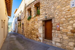 Une rue étroite bordée d’immeubles en pierre, de volets en bois et d’une enseigne indiquant un établissement proposant des chambres et le petit-déjeuner.